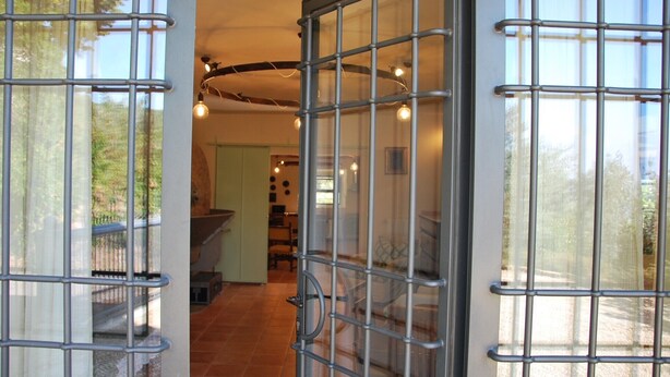 Een deuropening met metalen tralies, leidend naar een kamer met een betegelde vloer en een hangende lamp.