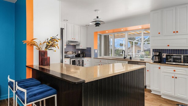Una cocina moderna con armarios blancos, una isla central y vistas al exterior.