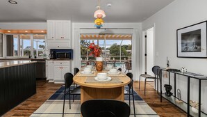 Una cocina moderna con armarios blancos, una zona de comedor con mesa de madera y vistas a una piscina a través de amplios ventanales.