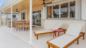 Un patio techado con mesa y sillas de comedor, una silla de descanso y un ventilador de techo.