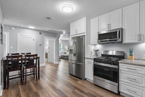 Una cocina moderna con armarios blancos, electrodomésticos de acero inoxidable y una mesa de comedor de madera con sillas.