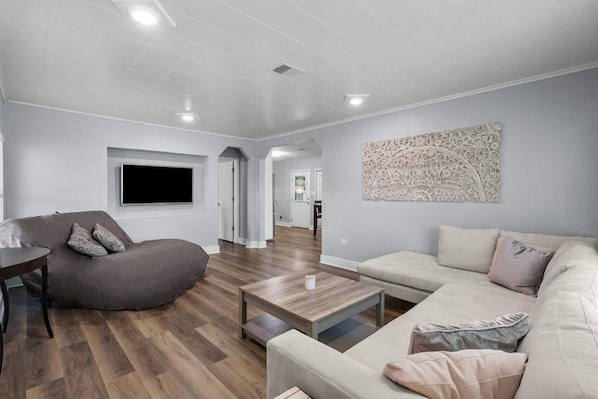 Una sala moderna con un sofá modular, un sillón de peluche, una mesita de centro y un televisor de pantalla plana montado en la pared.