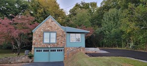 A stone and blue house with a garage, surrounded by trees and a driveway.