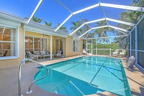 A covered outdoor swimming pool with lounge chairs and a glass-enclosed patio area.