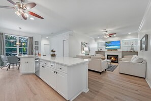 A modern kitchen with white cabinetry, a central island, and a dining area with a view of the outdoors.