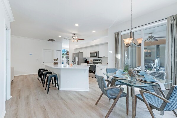 A modern kitchen with white cabinets, a central island, and a dining area with glass tables and blue chairs.