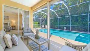 Ein moderner Raum mit einem in Glas eingefassten Pool, einer Couch, einem Couchtisch und Blick auf üppiges Grün.