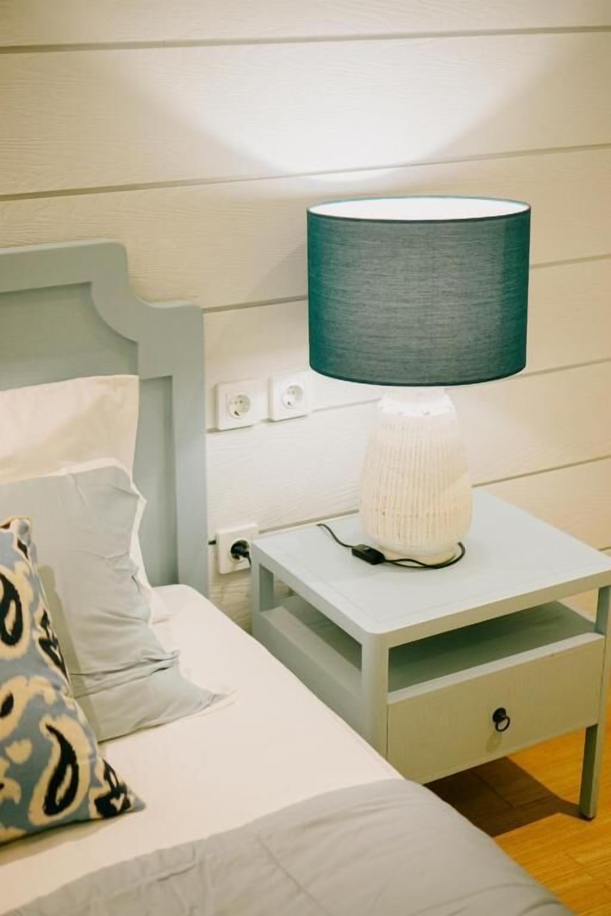 A neatly made bed with patterned pillows, a bedside table with a lamp, and a wall socket.