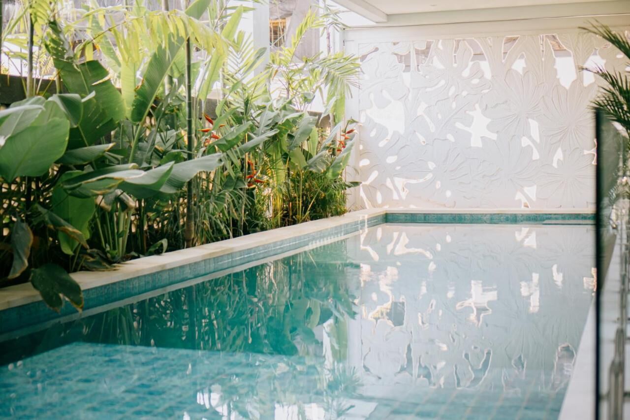 An indoor swimming pool with clear water, surrounded by lush tropical plants and a decorative white partition.