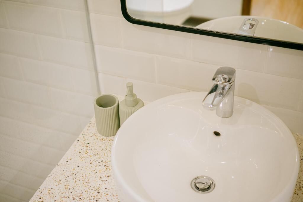 Une salle de bain avec un lavabo blanc, un miroir au-dessus et un comptoir à motifs.