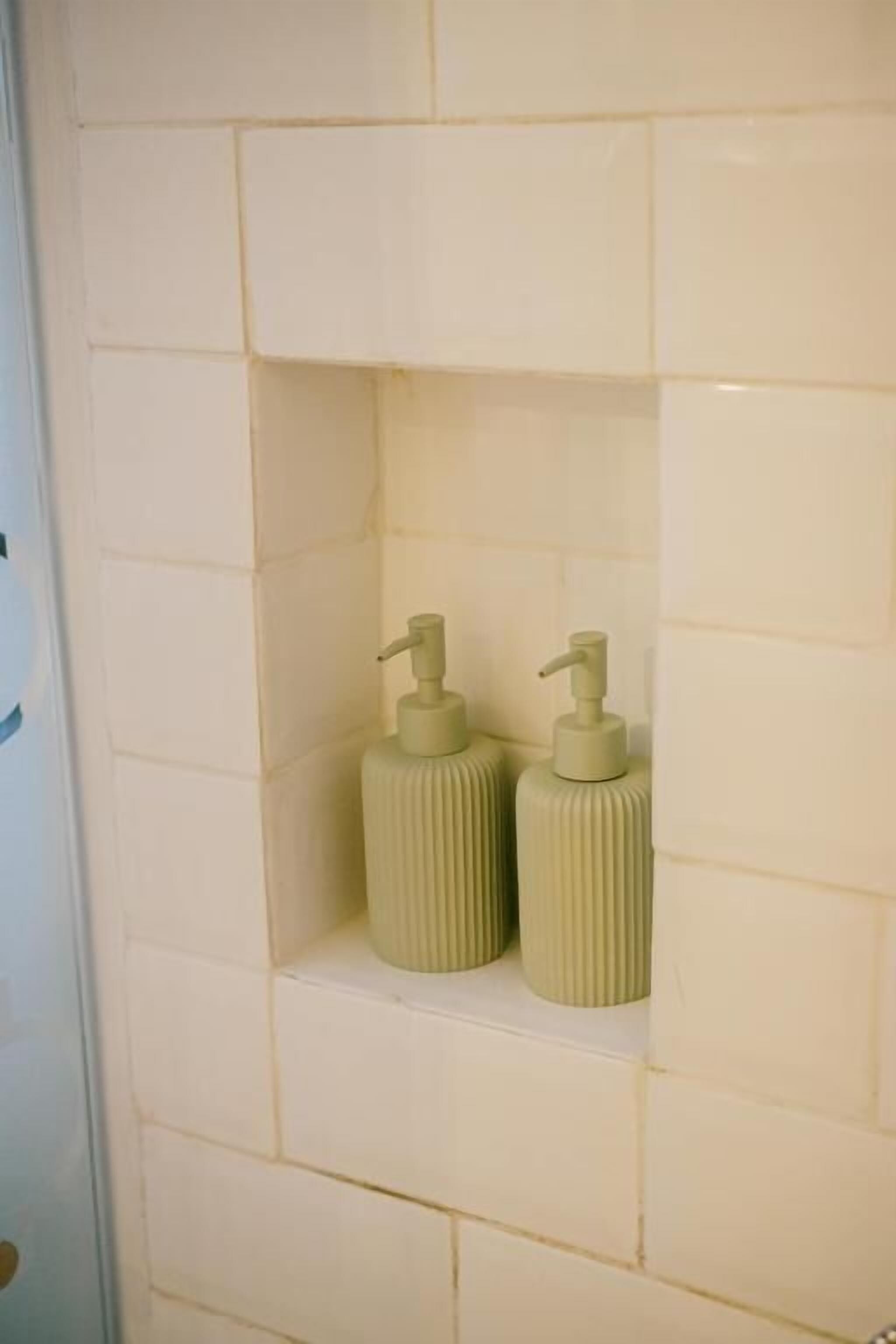 A bathroom with white tiles and two beige dispensers on a shelf.