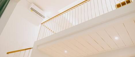 A multi-level interior with white walls, a wooden railing, and recessed lighting.