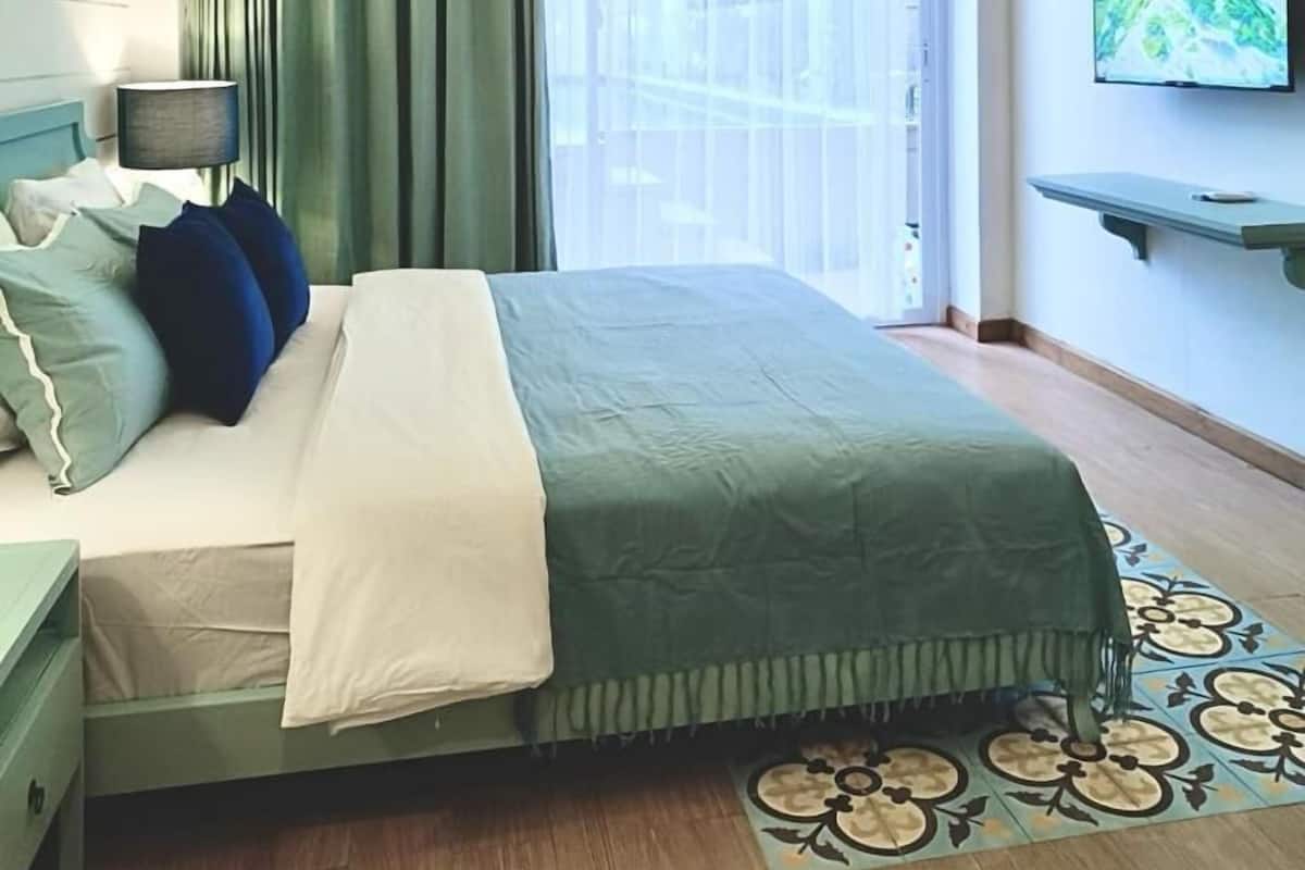 A modern hotel room with a bed, curtains, a TV, and a balcony view.
