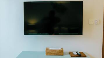 A flat-screen TV mounted on a wall above a light blue shelf with a basket and remote control.