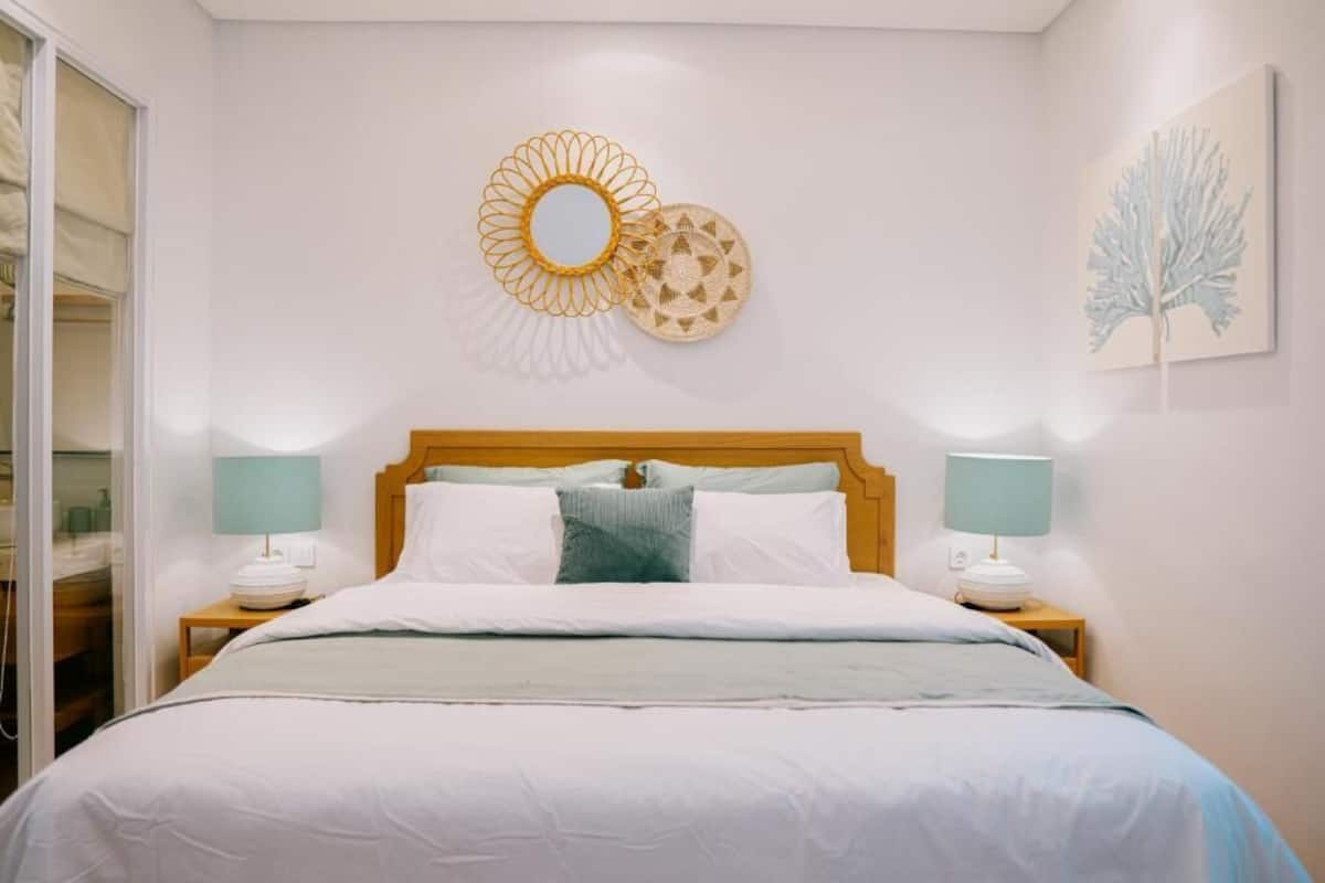 A neatly made bed with white bedding and a wooden headboard, flanked by two bedside tables with lamps.