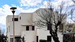 Un bâtiment moderne doté d’un toit plat, de nombreuses fenêtres et d’un jardin bien entretenu où l’on trouve diverses plantes et un arbre.