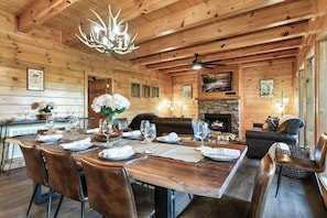 A wooden interior with a dining table set for six, a fireplace, and a ceiling fan.