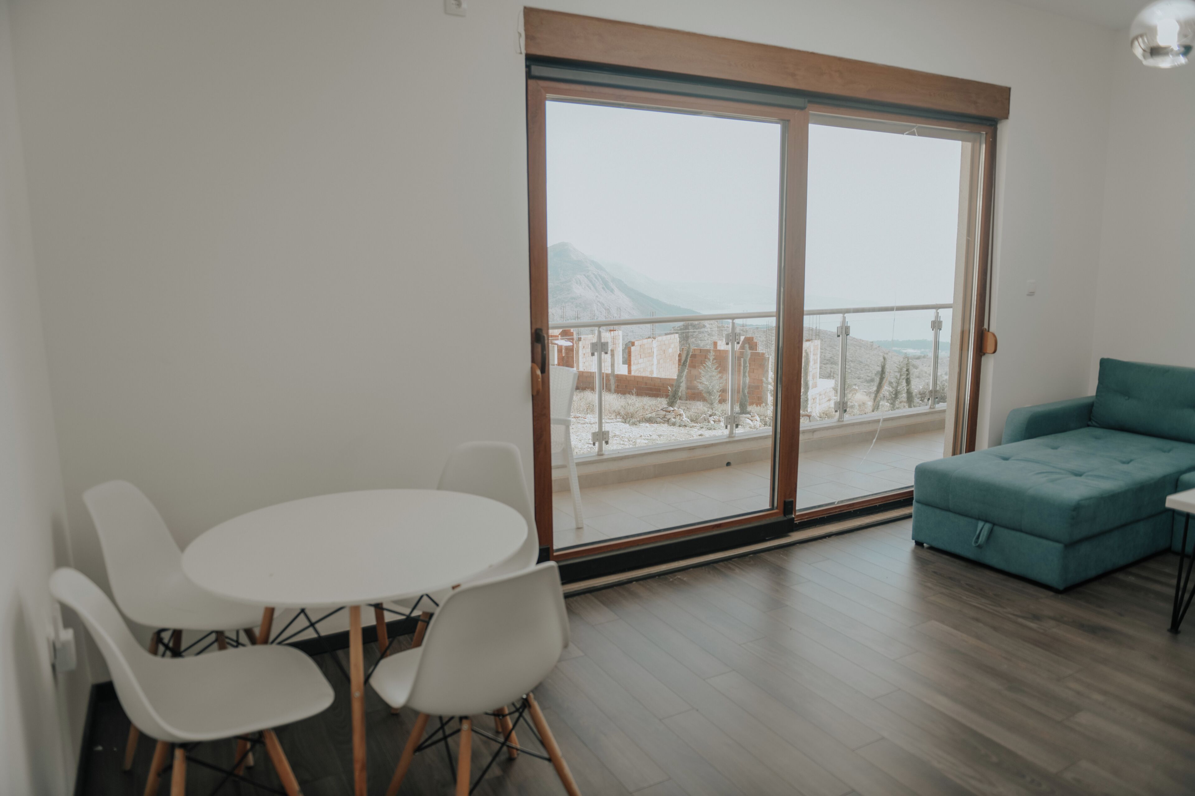 Uma sala de estar moderna com varanda, mobiliário branco e vista para uma paisagem montanhosa.
