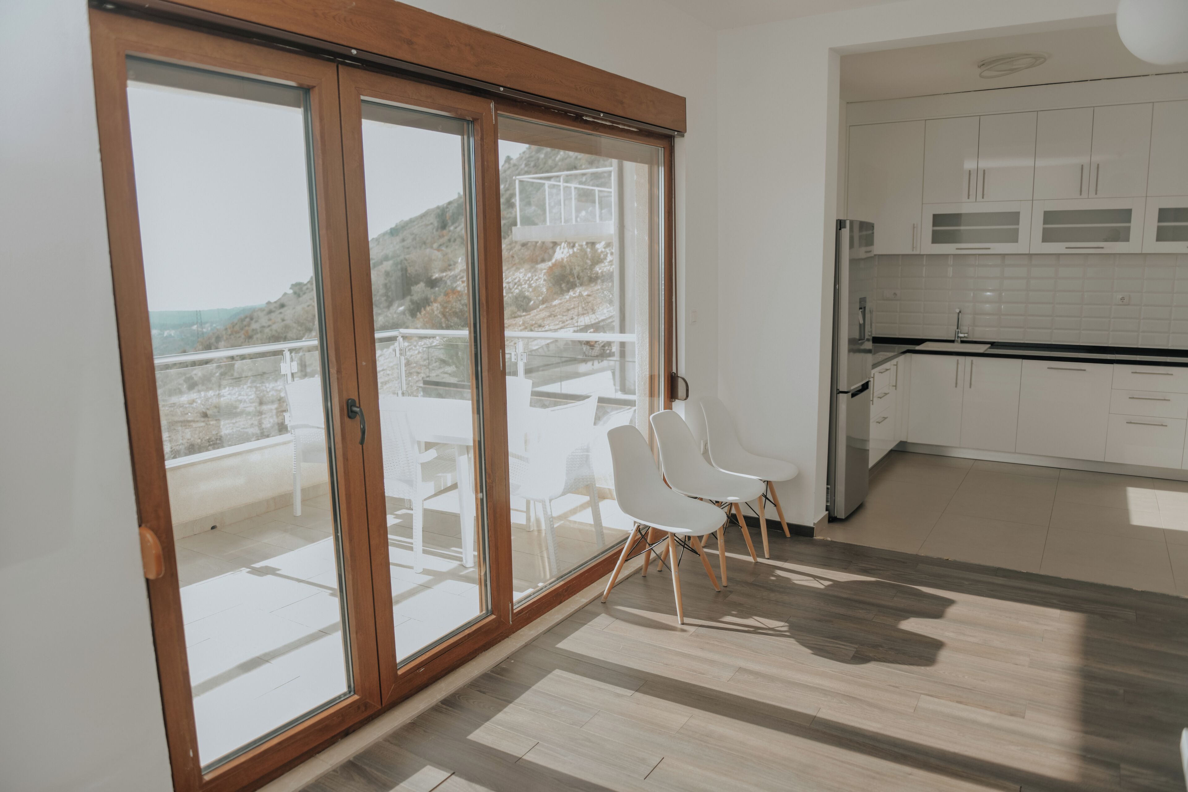 Une cuisine moderne avec des meubles blancs et une grande porte-fenêtre coulissante donnant sur un balcon.