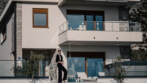 A modern two-story building with a balcony, outdoor seating, and a hanging chair. - Villa Dubrovnik Heights – Private pool and jacuzzi with sea view (Ivanica)