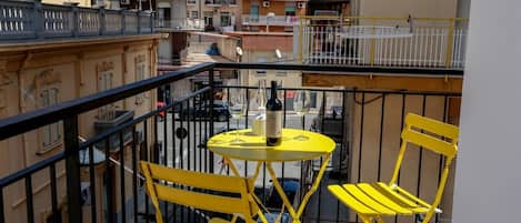 A balcony with yellow chairs and a small round table, overlooking a street with buildings.