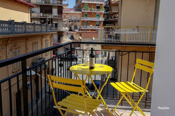 A balcony with yellow chairs and a small round table, overlooking a street with buildings. - Galliano 51. Holiday in Style – City Center (Soverato)