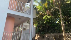 A multi-story building with balconies, surrounded by lush greenery and palm trees.