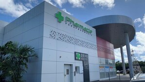 A pharmacy building with a green cross logo, a drive-through service sign, and a large water tank structure.