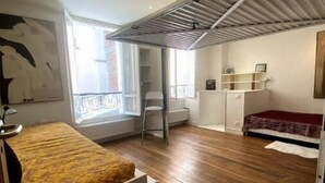 Et lille værelse med seng, radiator, vindue og balkon.