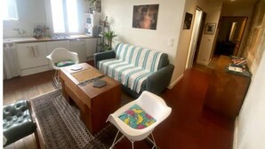 En kompakt opholdsstue med tekøkken, en stribet sofa, et spisebord og en lille, hvid stol.