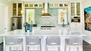 A modern kitchen with a large island, white cabinetry, and a stone backsplash. - Toes in the Water (Rosemary Beach)