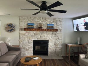 Una sala de estar con chimenea de piedra, ventilador de techo, televisor y sofá.