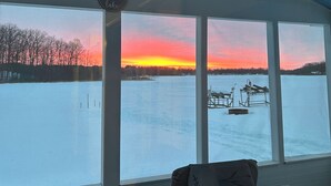 Ein Zimmer mit großem Fenster mit Blick auf einen zugefrorenen See bei Sonnenuntergang.