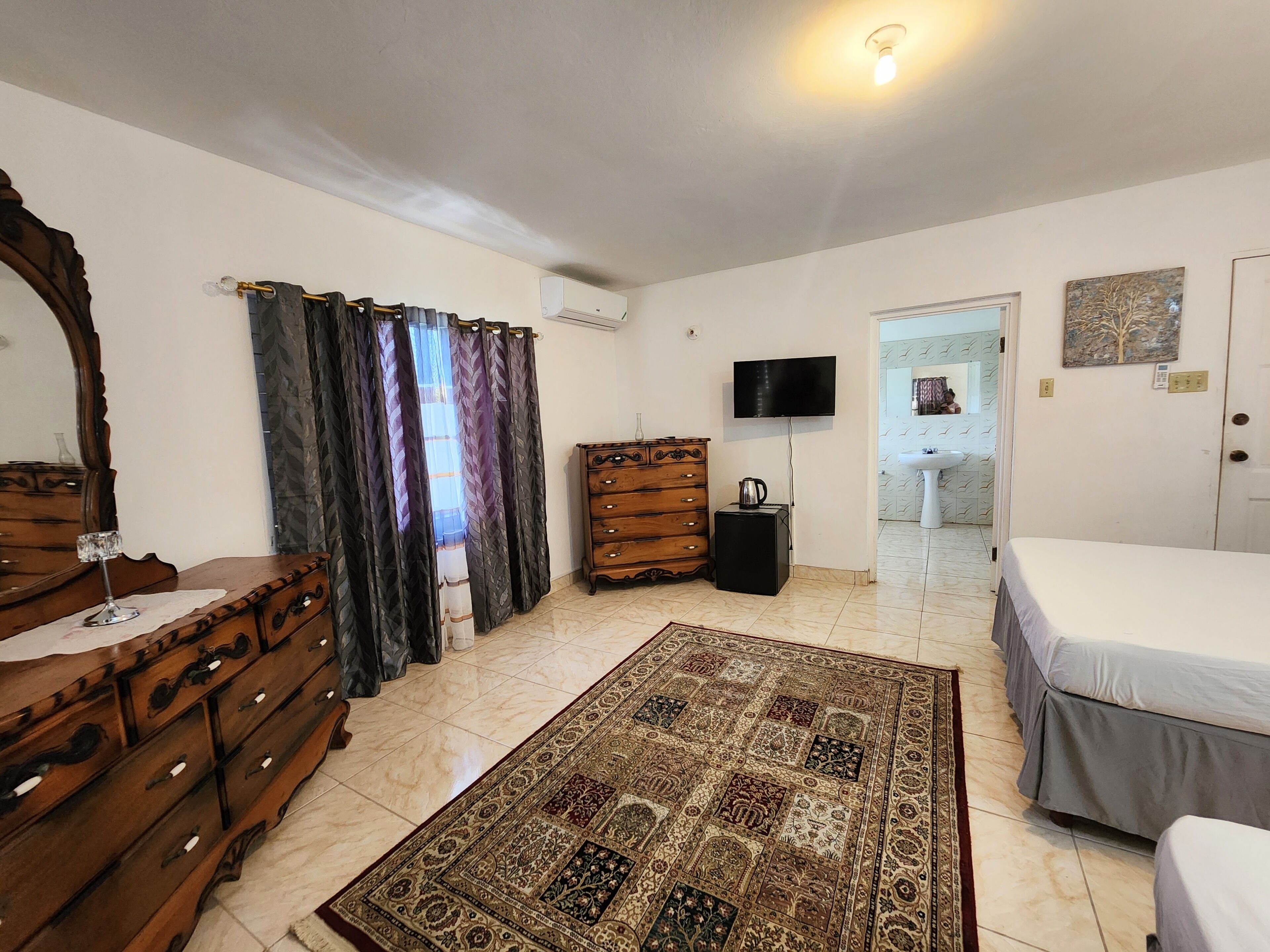 A bedroom with a bed, a dresser, a television, and a bathroom visible through an open door.