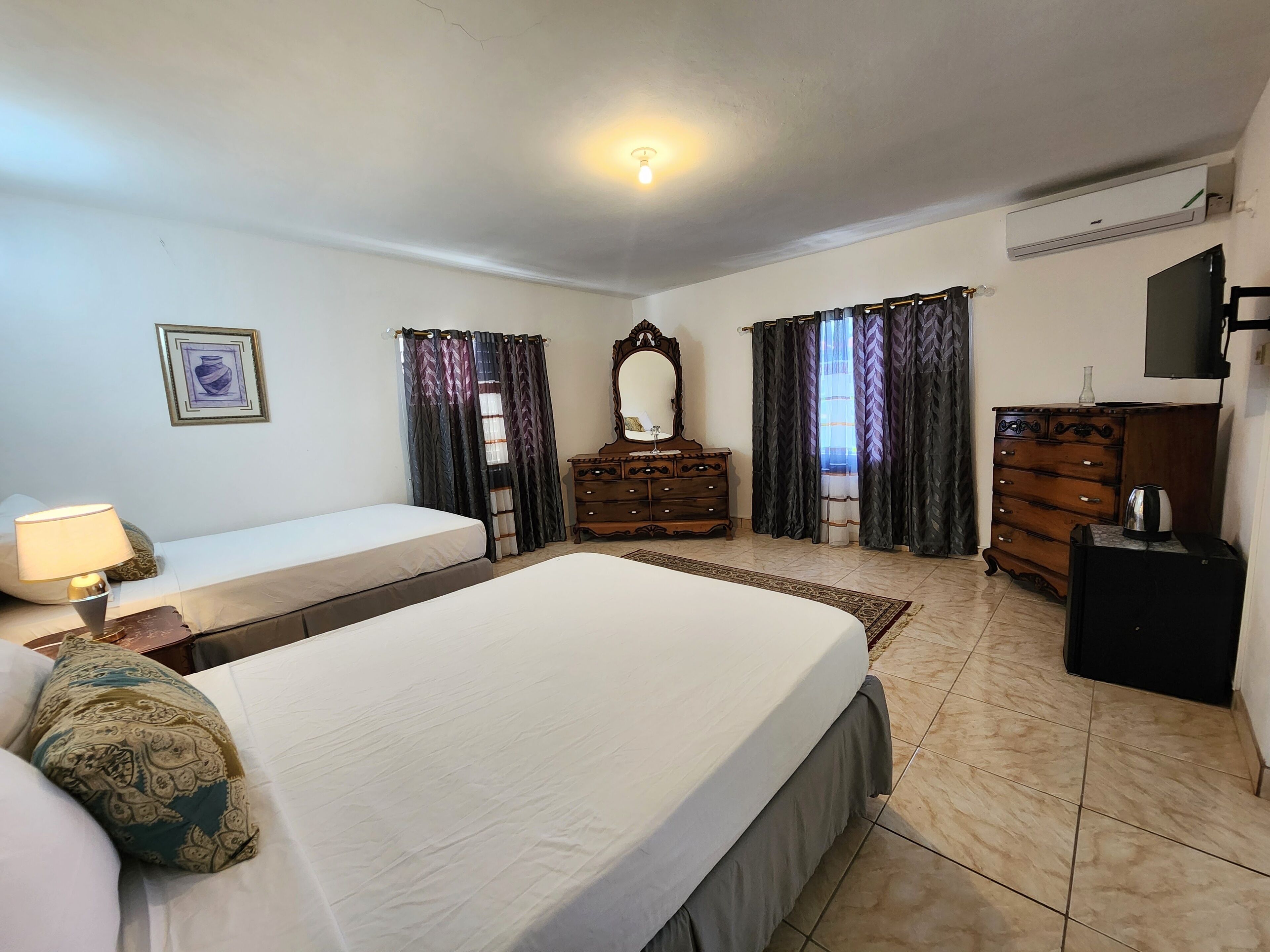 Une chambre d’hôtel avec un lit, une commode, un miroir, une télévision et une fenêtre avec des rideaux.
