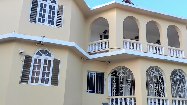 A multi-story building with balconies, a red door, and a parked car. - Apartment 379 Hudson Avenue (Montego Bay)