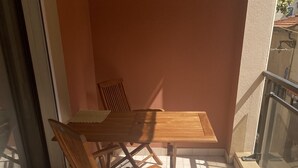 Puisesta pöydästä ja tuoleista koostuva kalusto laatoitetulla parvekkeella, jossa on lasikaide.