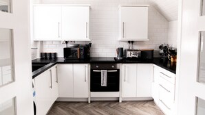 A modern kitchen with white cabinets, a black countertop, and a herringbone-patterned floor. - 3 Bed House - Sleeps 6 - Garden - Parking - Wifi (Manchester)
