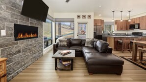 A modern living room with a stone fireplace, leather sofa, and a dining area with a kitchen in the background. - Mountain townhouse w/ hiking, biking & adventure (Granby)