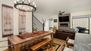 A modern living room with a wooden dining table, a brown leather sofa, and a stone fireplace. - Mountain townhouse w/ hiking, biking & adventure (Granby)