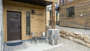 A wooden exterior with a brown door, stone pillar, and two metal chairs outside. - Mountain townhouse w/ hiking, biking & adventure (Granby)