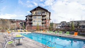 A swimming pool with lounge chairs and tables, surrounded by a building with multiple balconies. - Mountain townhouse w/ hiking, biking & adventure (Granby)
