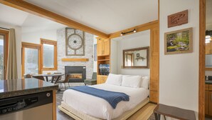 Een moderne slaapkamer met een groot bed, houten balken, een stenen open haard en een eethoek met uitzicht.