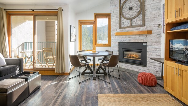 Een moderne woonkamer met een open haard, een eettafel met stoelen, een bank en een balkon met uitzicht op bomen.