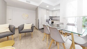 Ein modernes, helles Wohnzimmer mit einem Glastisch, grauen Sofas und einem gelben Beistelltisch.