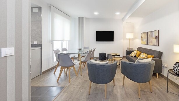 Ein modernes Wohnzimmer mit einer Couch, Sesseln, einem Couchtisch und einem flachbildfernseher an der Wand.