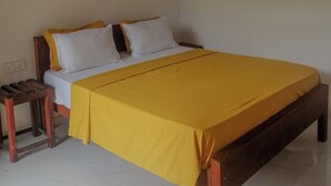 A single bed with a yellow bedspread, white pillows, and a wooden headboard. There is a small wooden nightstand beside the bed. - Sinharaja Serenity Retreat (Deniyaya)