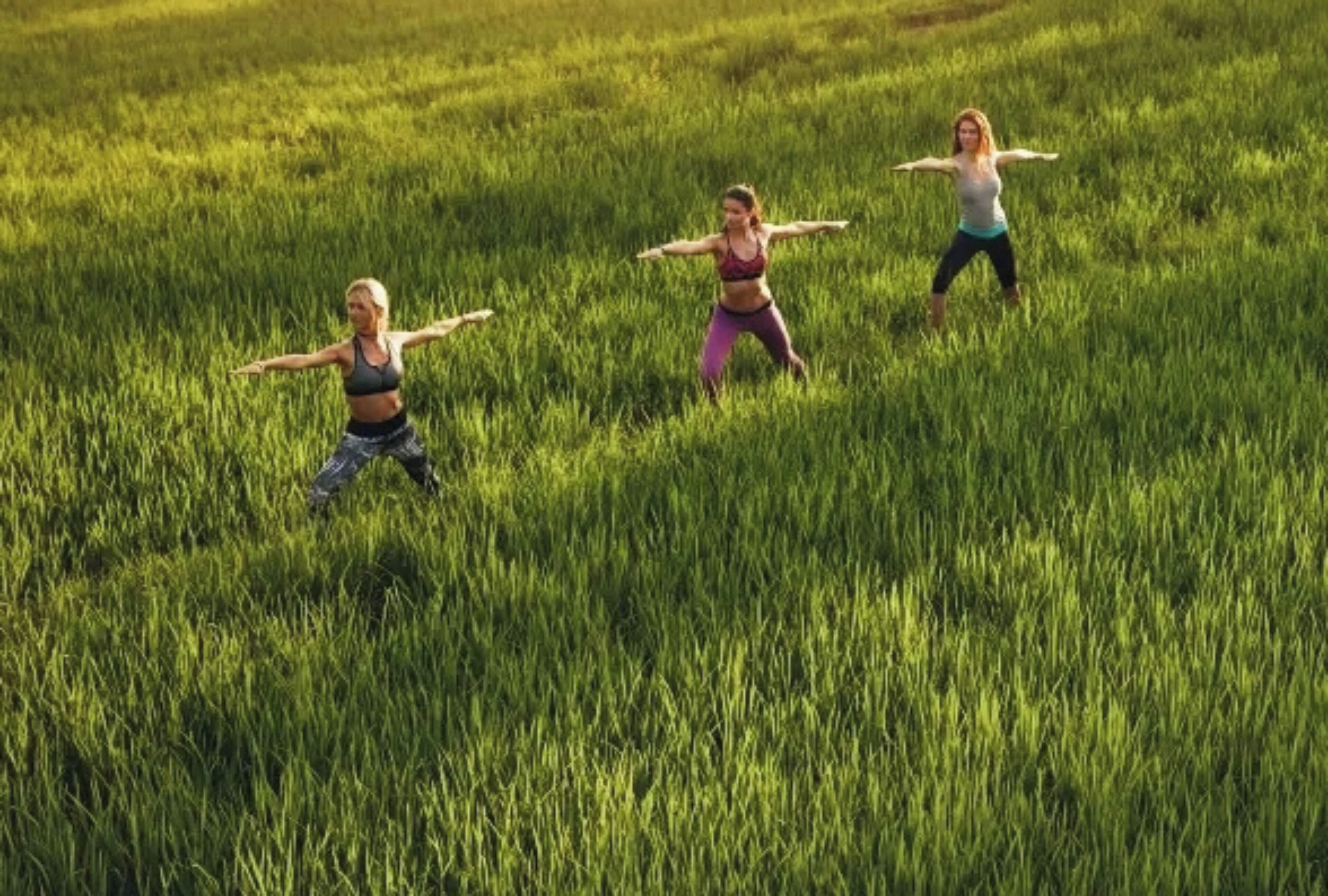 Tres personas realizando una postura de yoga en un campo cubierto de hierba.