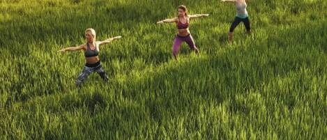 Tres personas realizando una postura de yoga en un campo cubierto de hierba.