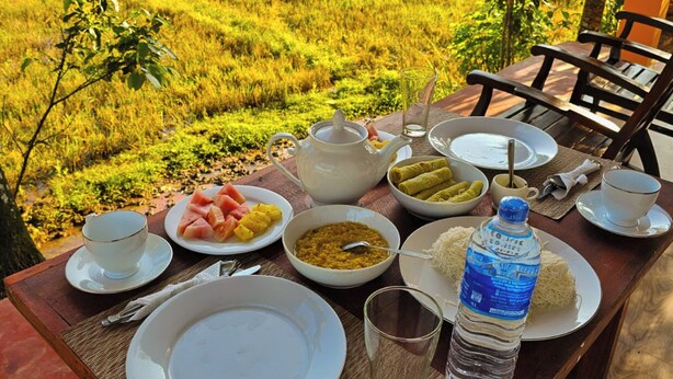 A table set for breakfast with a view of a lush green field. - Sinharaja Serenity Retreat (Deniyaya)